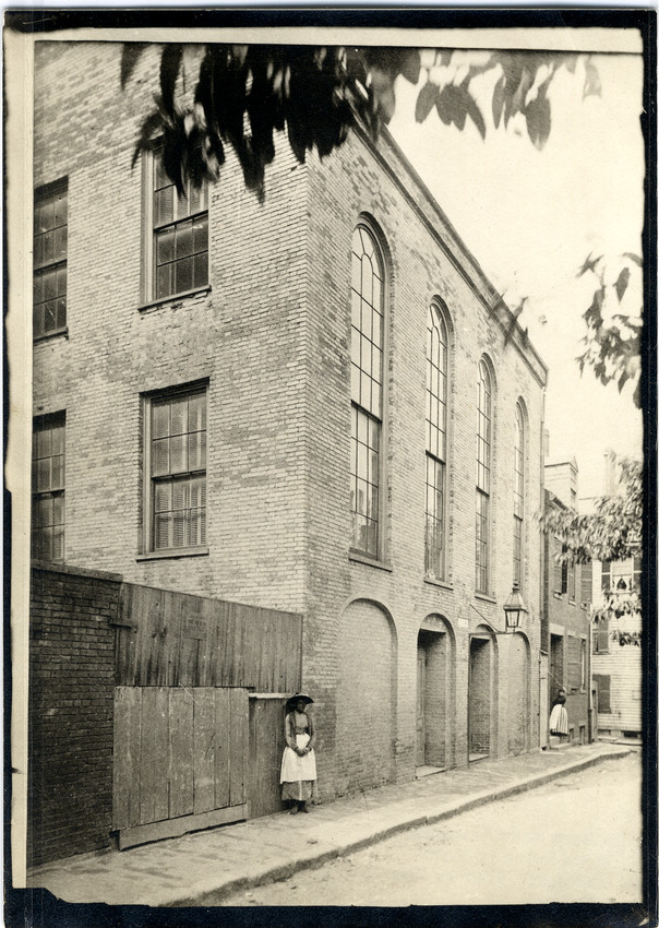 A woman stands in front of a large brick building