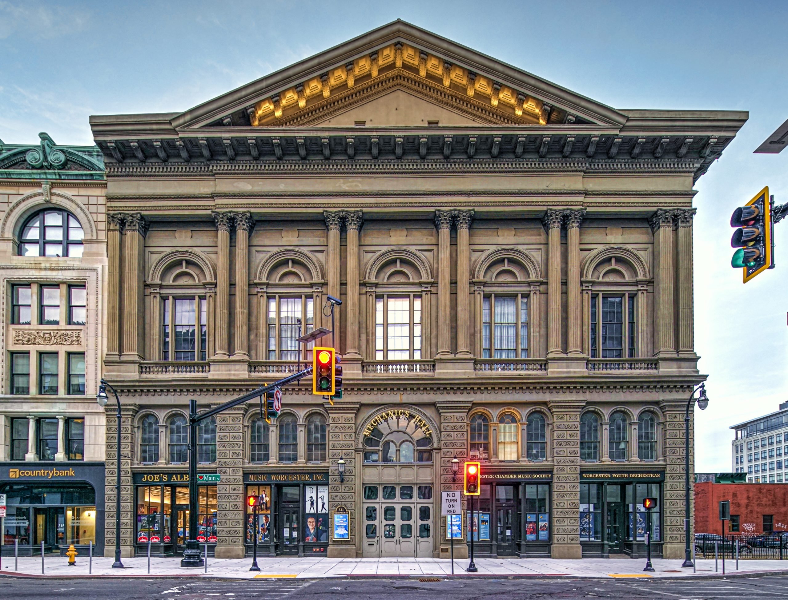 Columned facade of Mechanics Hall, Worcester with traffic lights in the foreground. Storefronts are visible at street level.