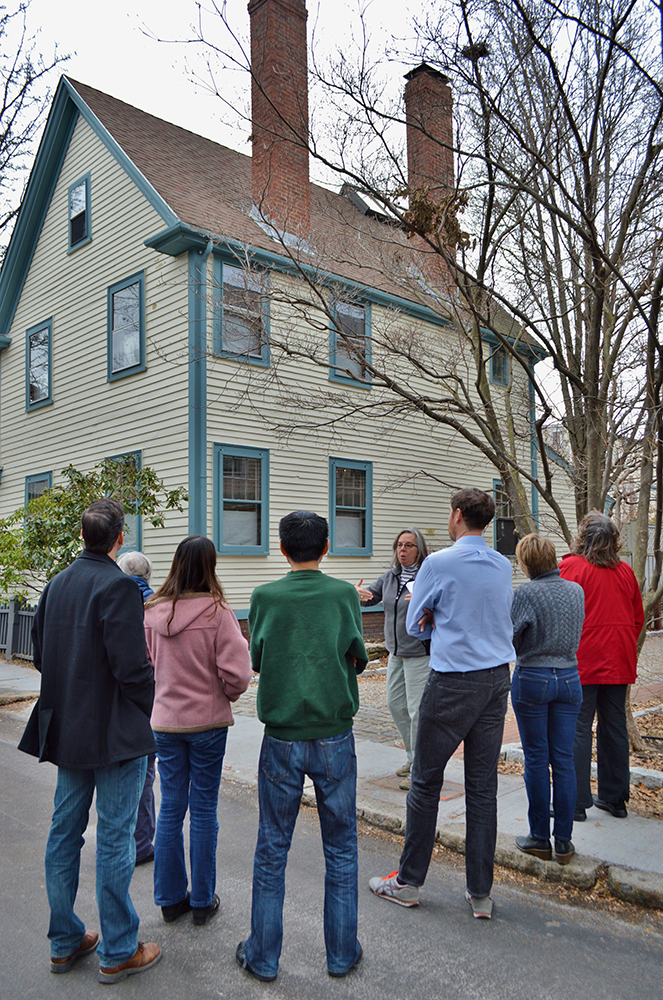 Group of eight people in front of house with green siding.