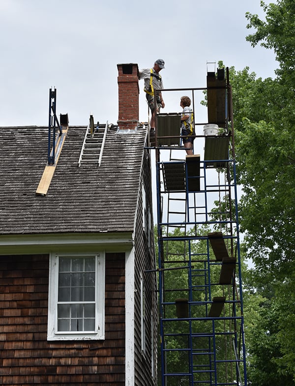 Brown shingled house with scaffolding. Roof and Chimney repair.