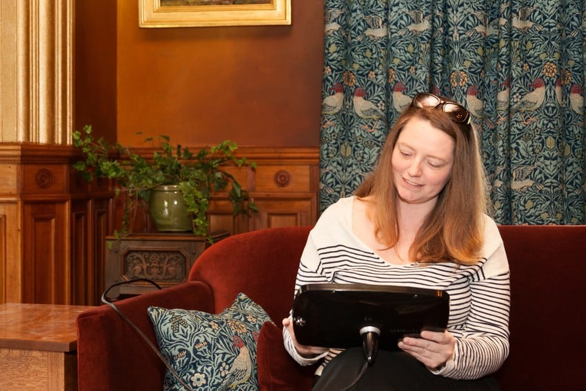 Woman seated on a sofa in a Victorian interior using a tablet.