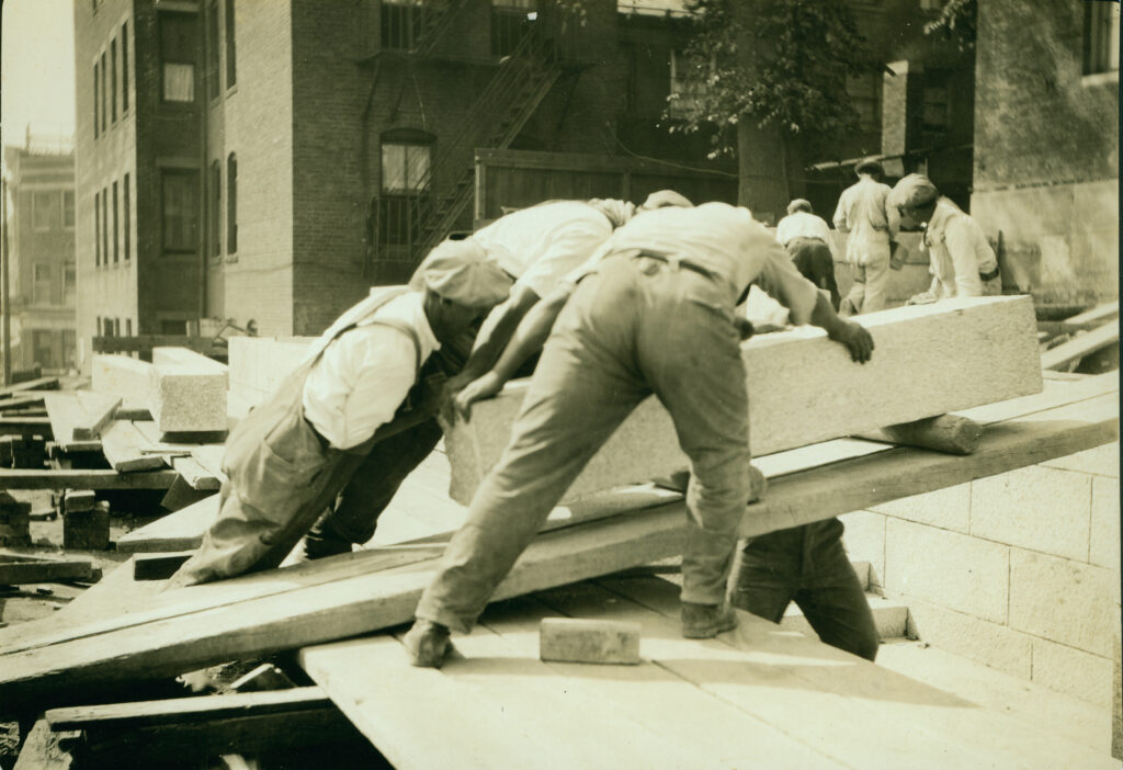 Workers moving a large stone block on a construction site.